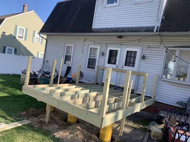 Partially built wooden deck on yellow supports, attached to a light-colored house.
