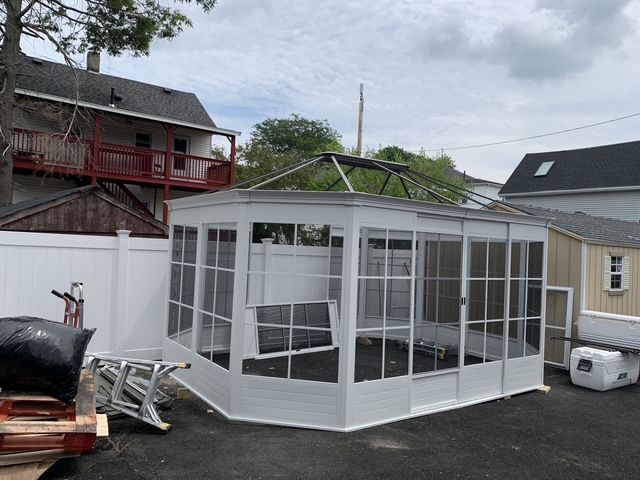 White screen room with a missing window frame, near a white fence and buildings.