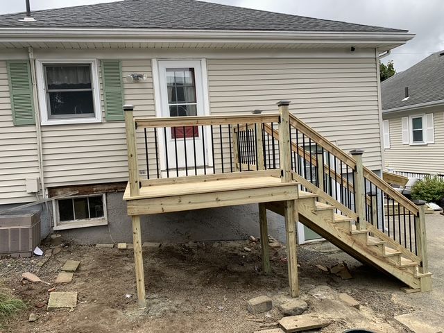 A wooden deck with black railing and stairs leading down from a light-colored house.
