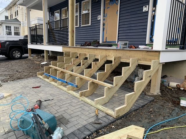 Construction of wooden steps leading up to a blue house with a black railing. A level lies on the steps.