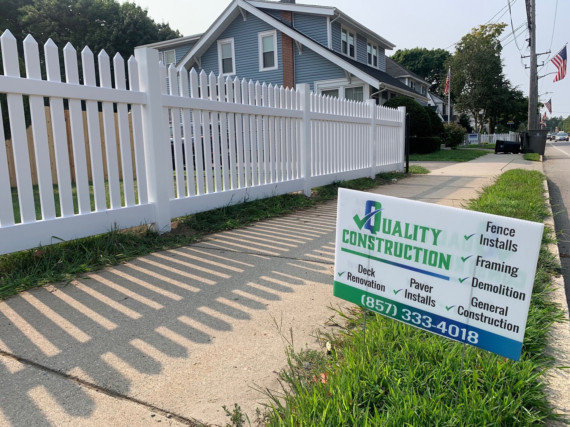 White picket fence in front of a house with a construction sign, on a sunny day.