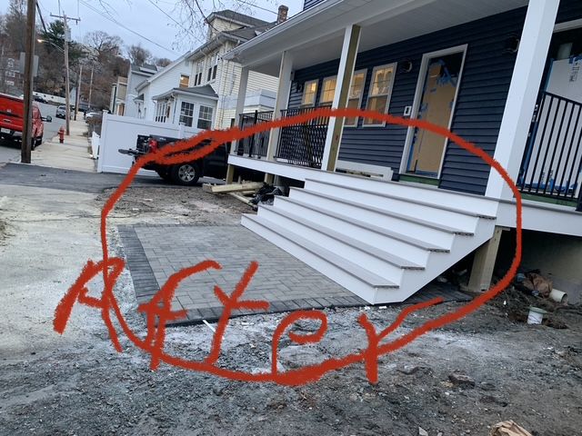 Newly constructed exterior steps of a blue house. White stairs lead to a porch. Paved area in foreground.