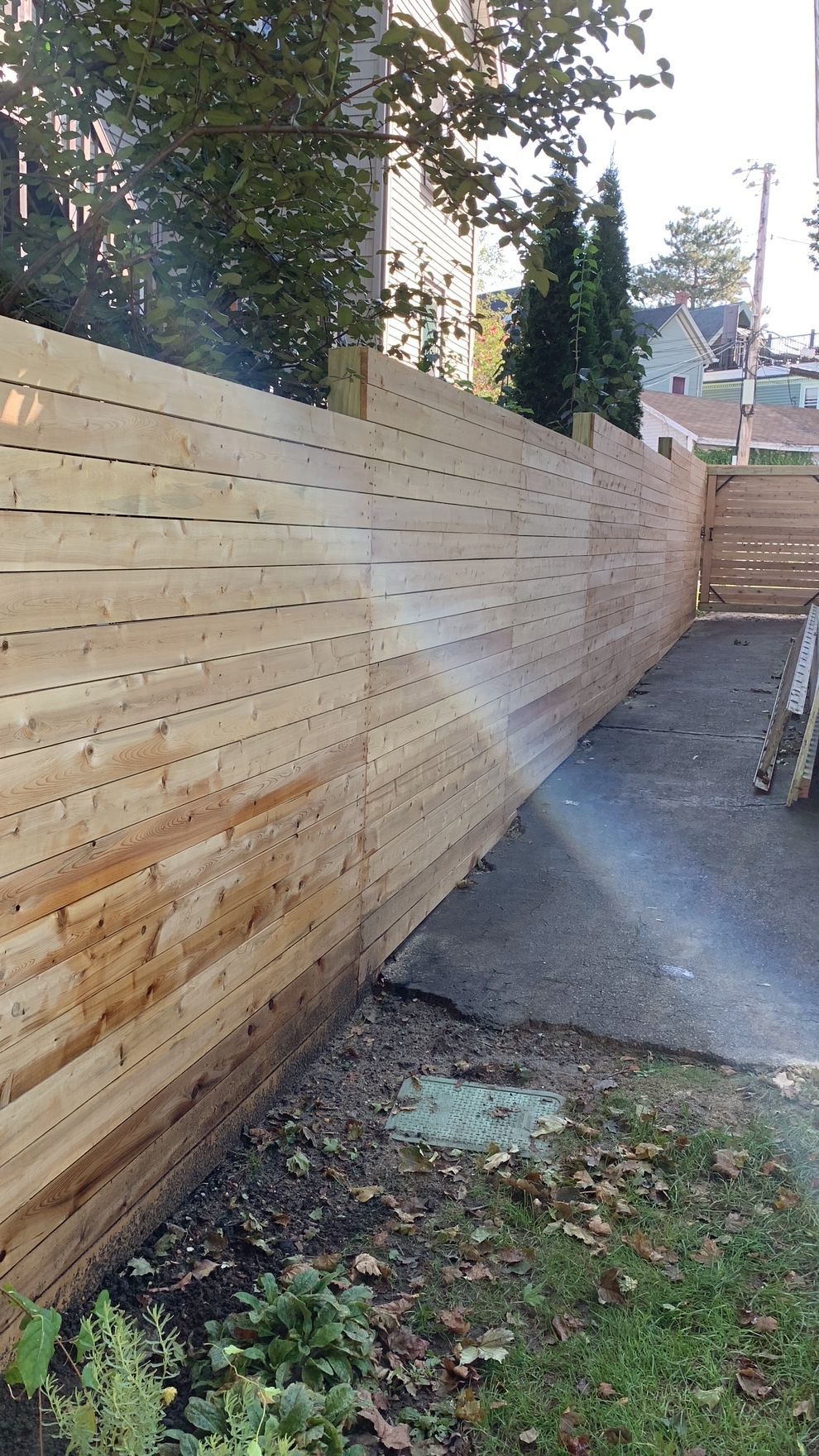 Wooden fence in a residential area, with a grassy yard and asphalt pathway.