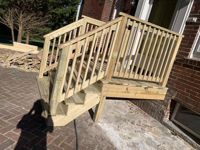 Wooden outdoor deck with stairs attached to a brick building. Handrails and a landing are visible.