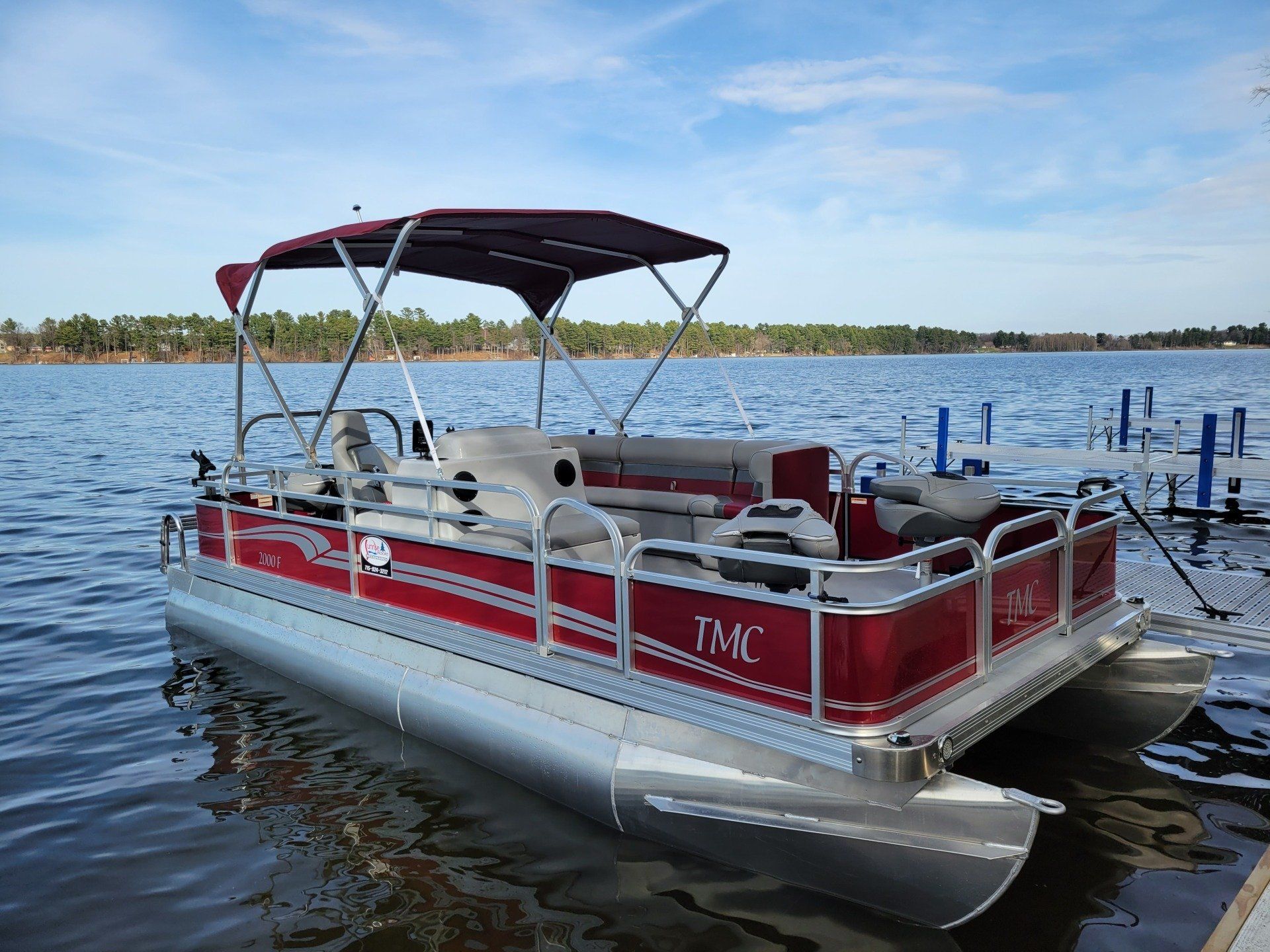 A red pontoon boat is docked at a dock on a lake.