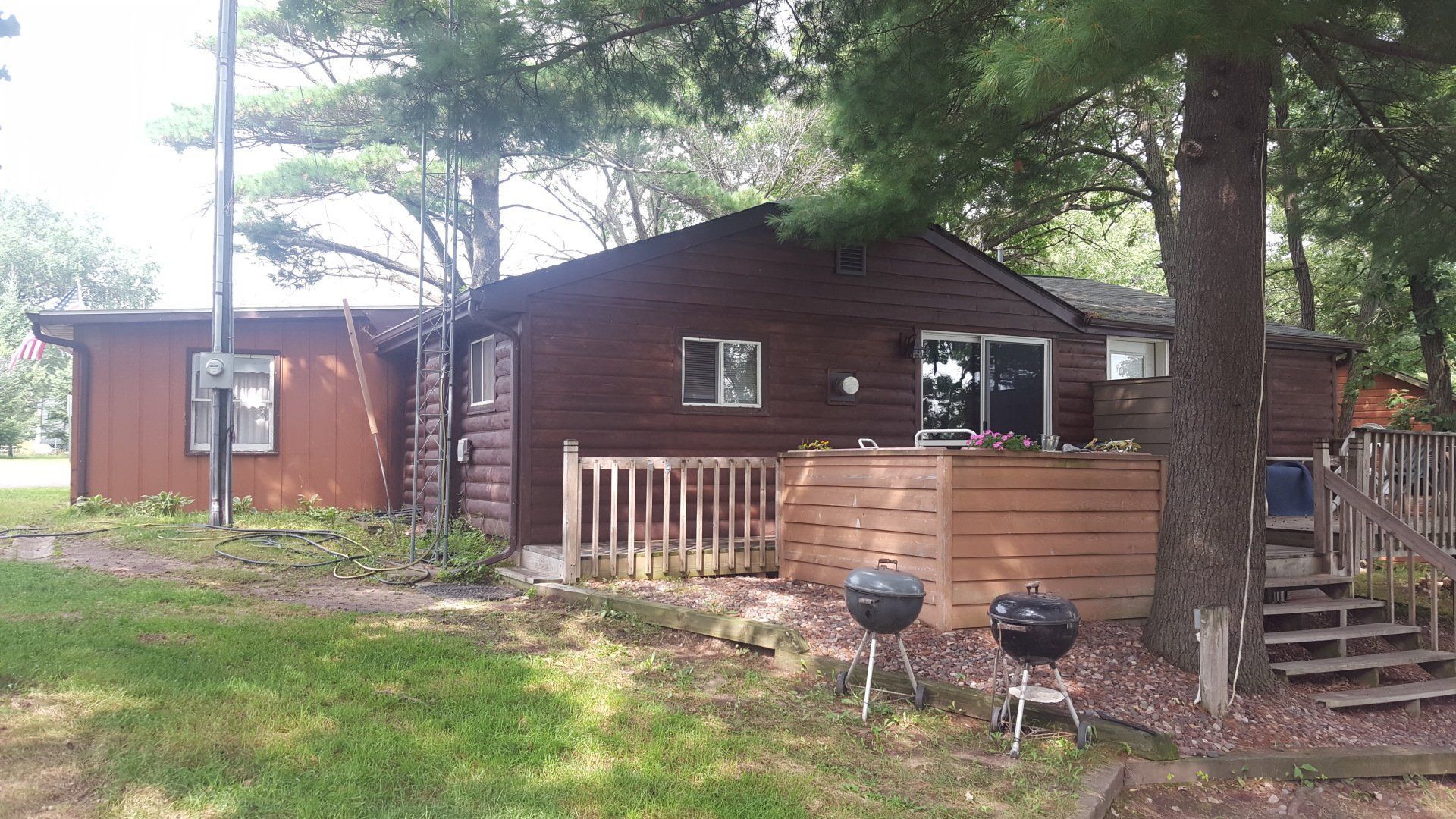 A wooden house with a deck and two grills in front of it.