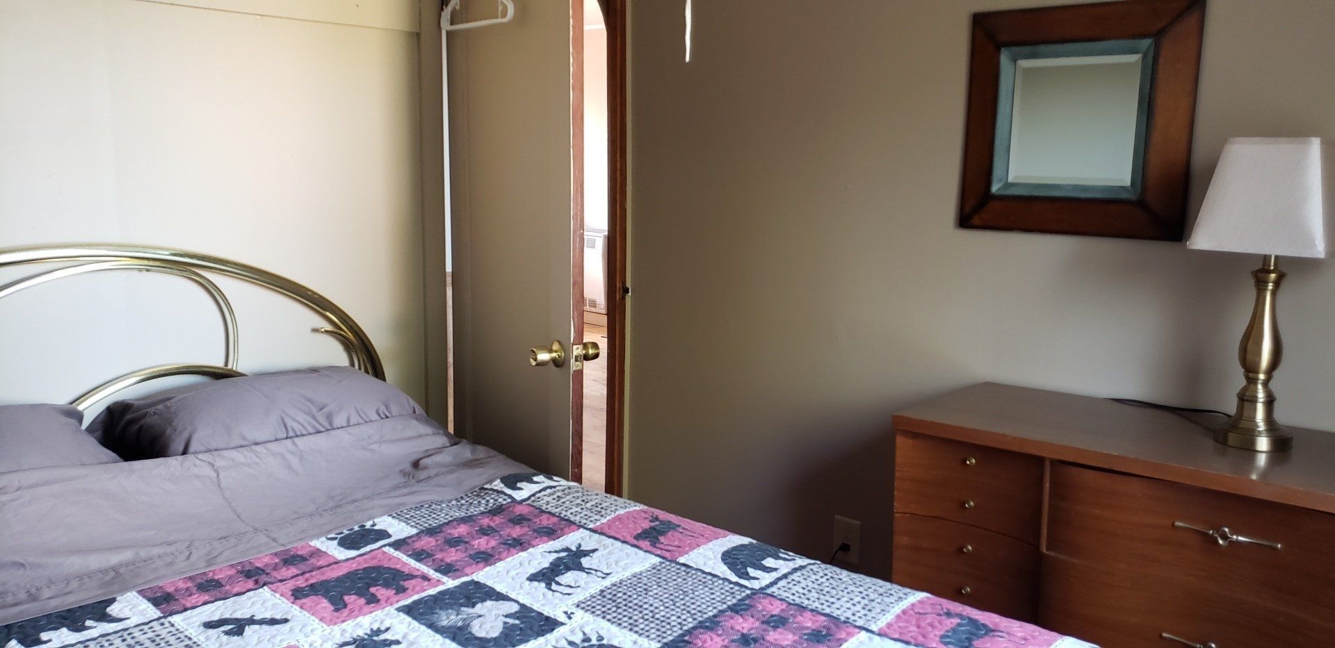 A bedroom with a bed , dresser , lamp and mirror.