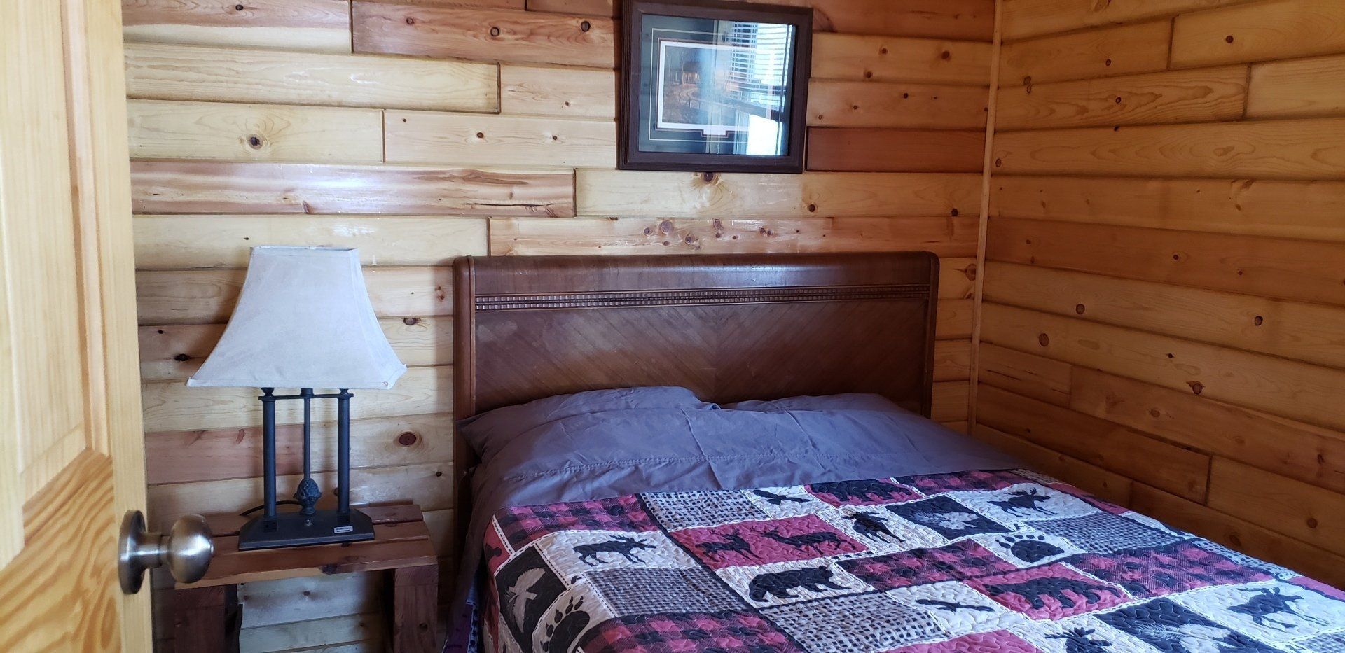 A bedroom in a log cabin with a bed and a lamp.