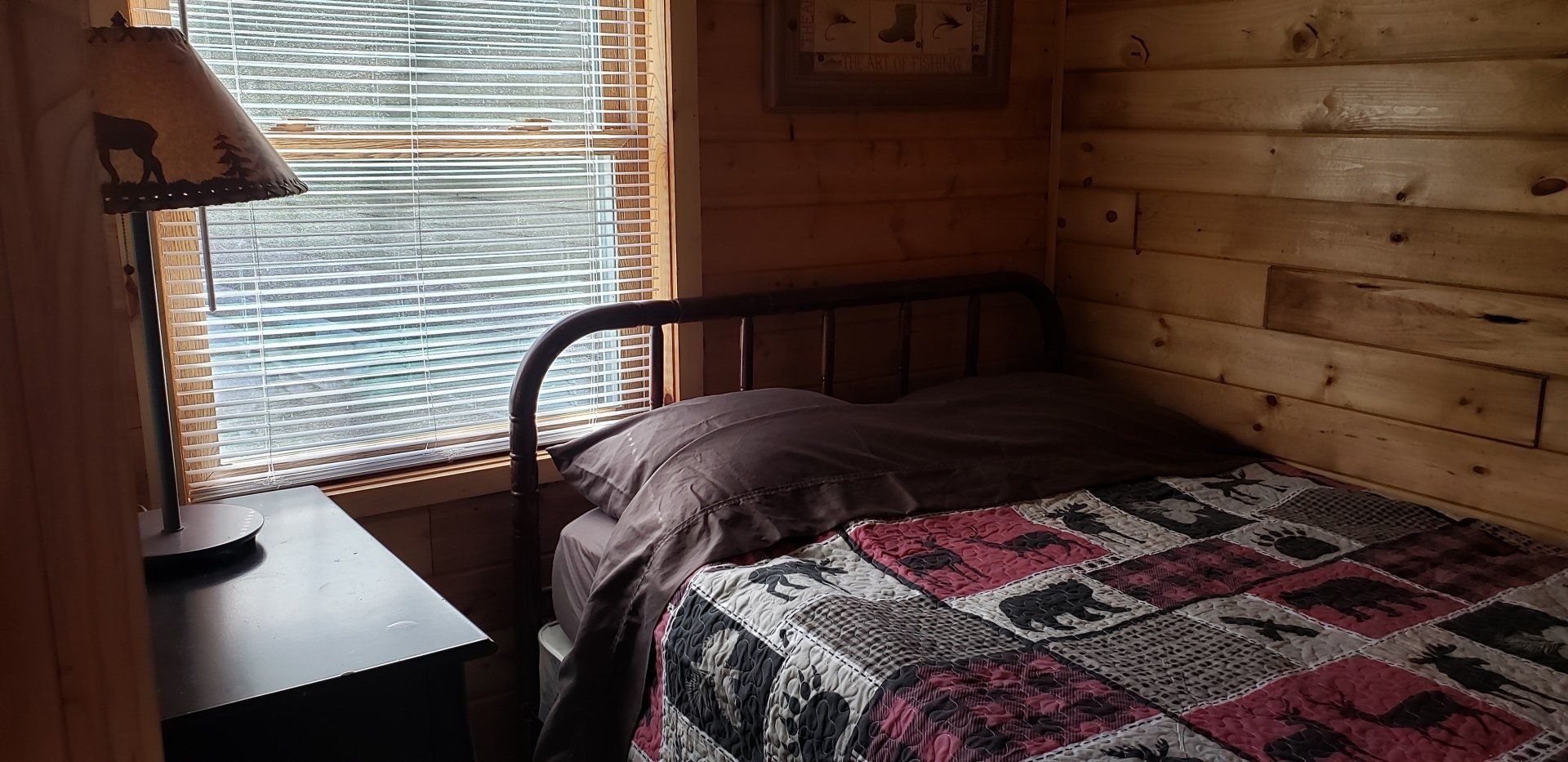 A bedroom with a bed , nightstand , lamp and window.