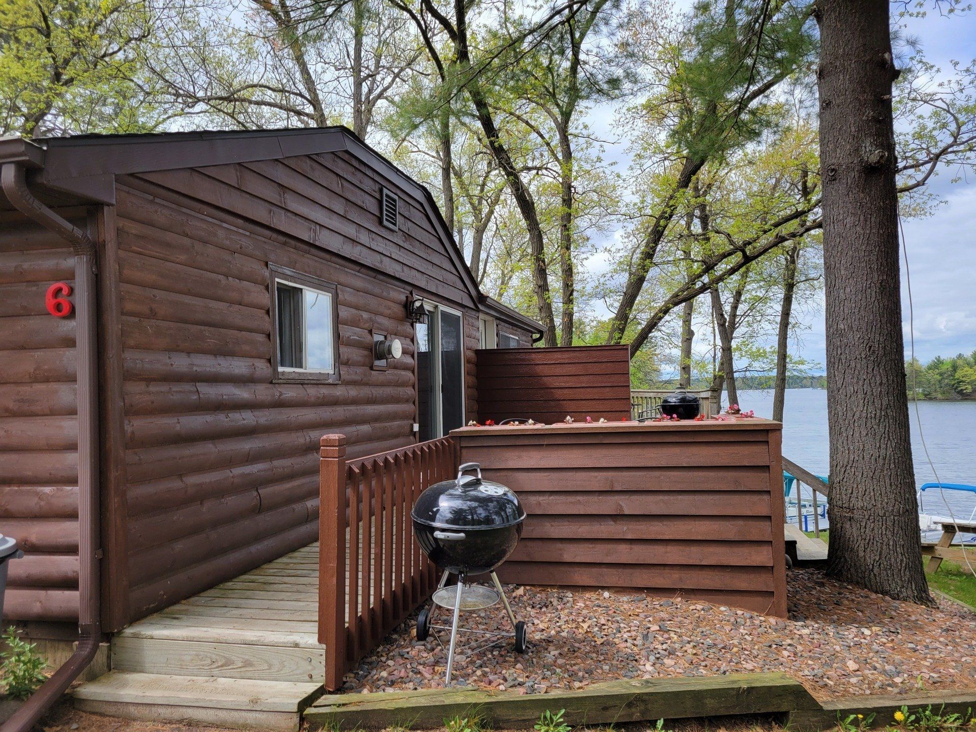 A log cabin with a grill on the deck next to a lake.