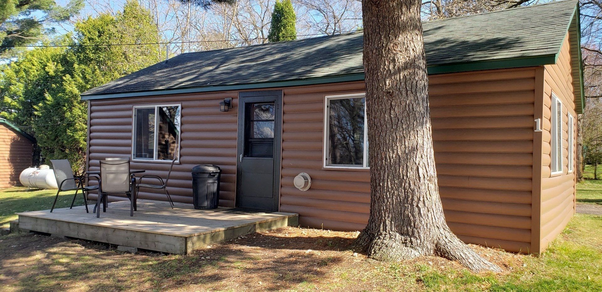 A small brown house with a deck and a tree in front of it.