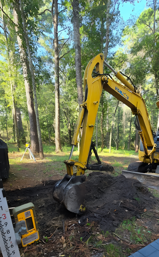 Yellow excavator digging in dirt, trees in the background.