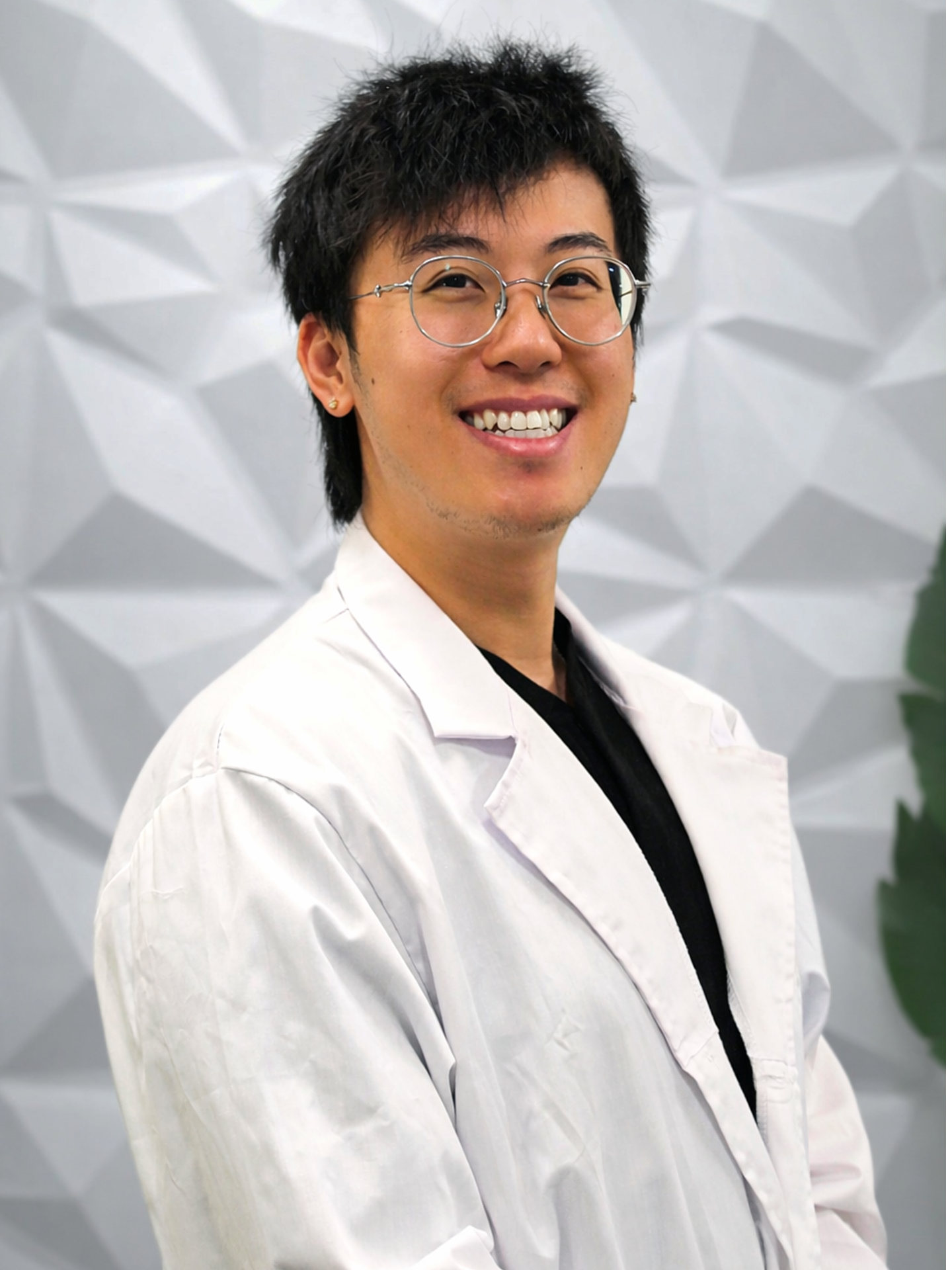 A professional in a white lab coat and glasses smiling against a textured, light-colored geometric background.
