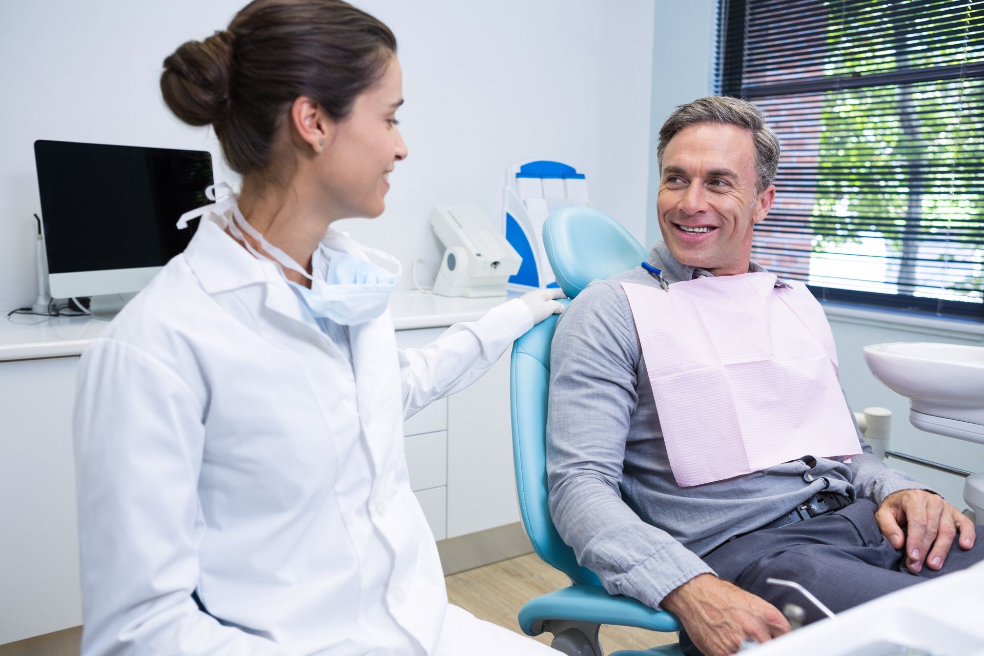 Dentist and patient in a dental office. Dentist in white coat gestures, patient smiles.