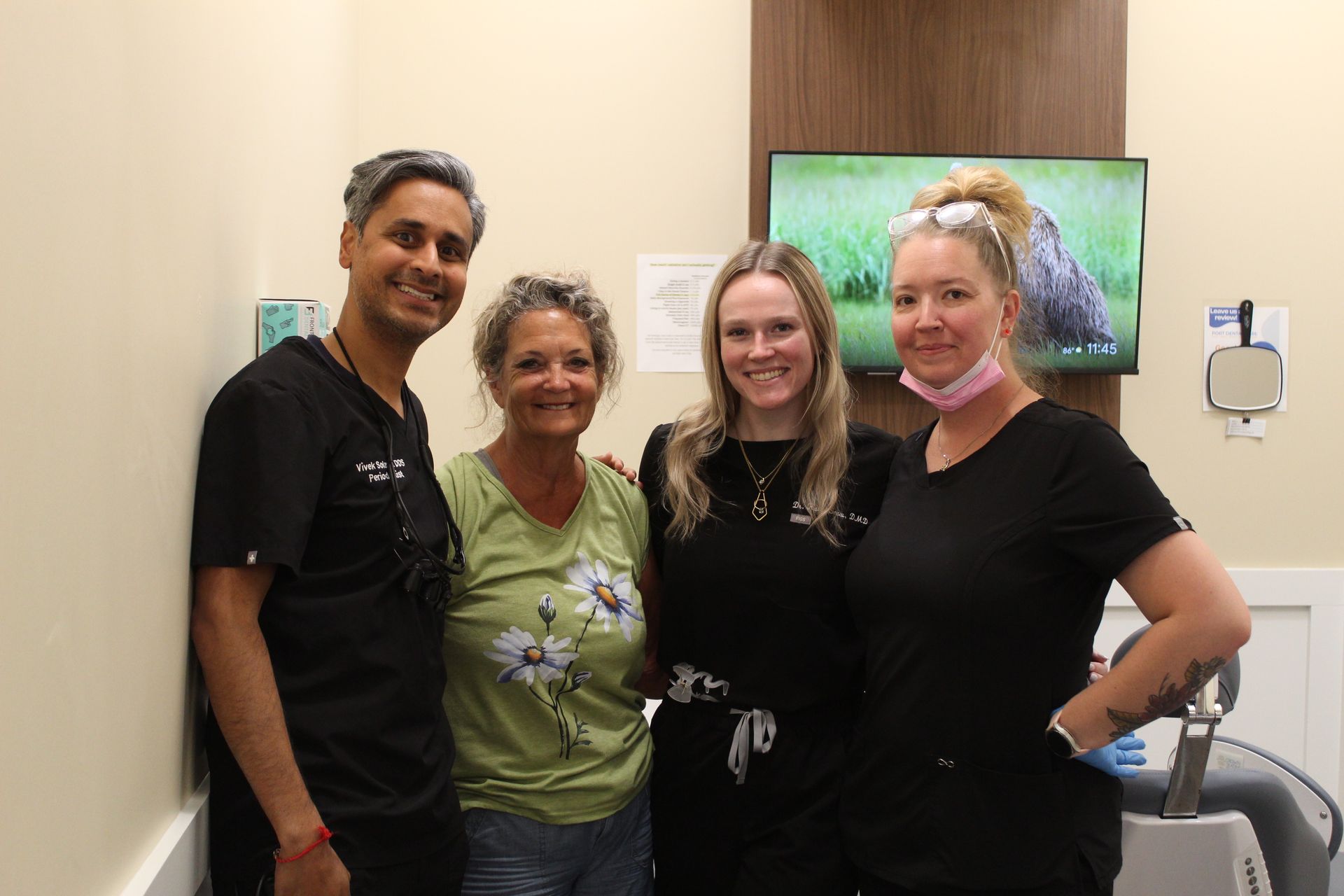 Four people smiling, posing in a dental office. A woman in a green shirt smiles with a group.