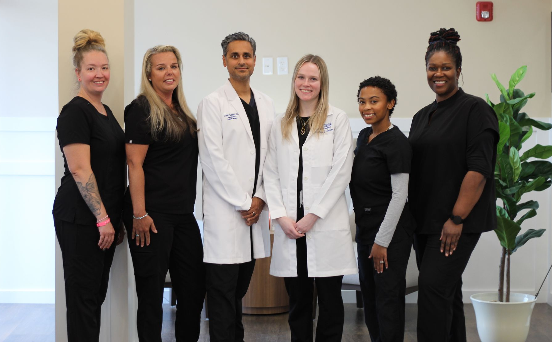 Six medical professionals in a clinic setting, wearing scrubs or lab coats, smiling at the camera.