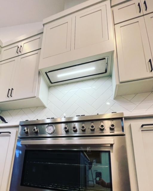 Empty kitchen with cream cabinets, grey countertops, and a stainless steel range hood.