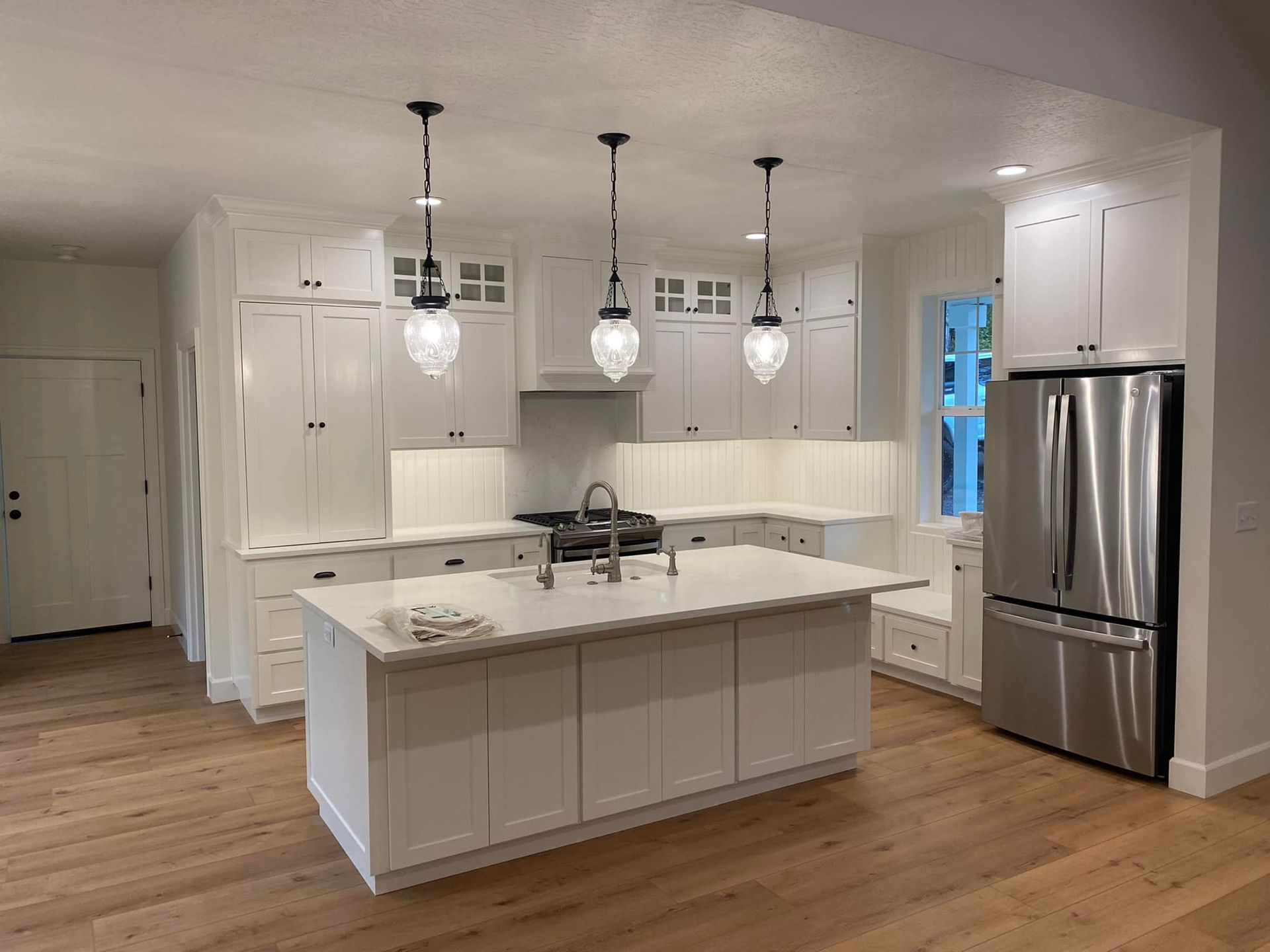 Modern kitchen with a large island, light wood cabinets, and a glass-door pantry, opening to an outdoor patio.