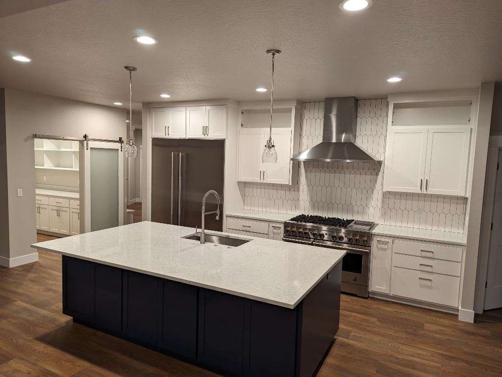 Narrow kitchen with light wood cabinets, granite countertops, and a stove. A dining table is in the foreground, with a doorway to a library in the back.