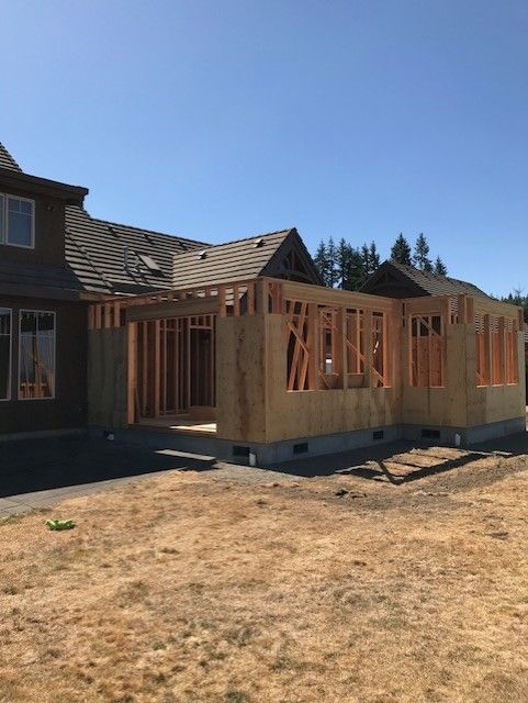 Interior room under construction, white walls with exposed electrical outlets, doorway to a green outdoor view, wooden floor.