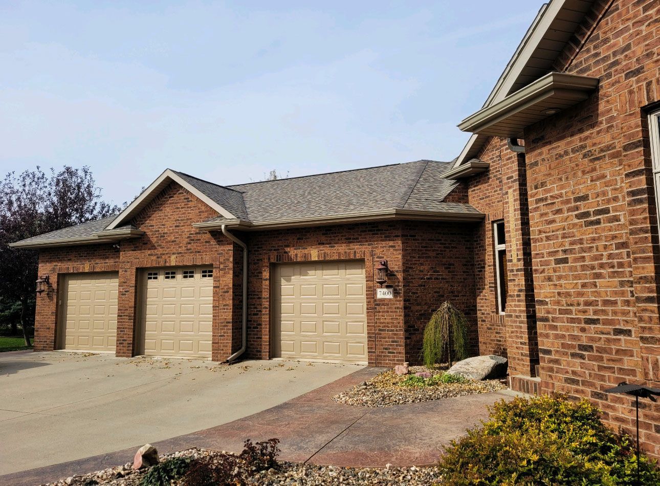 a brick house with three garage doors and a driveway .