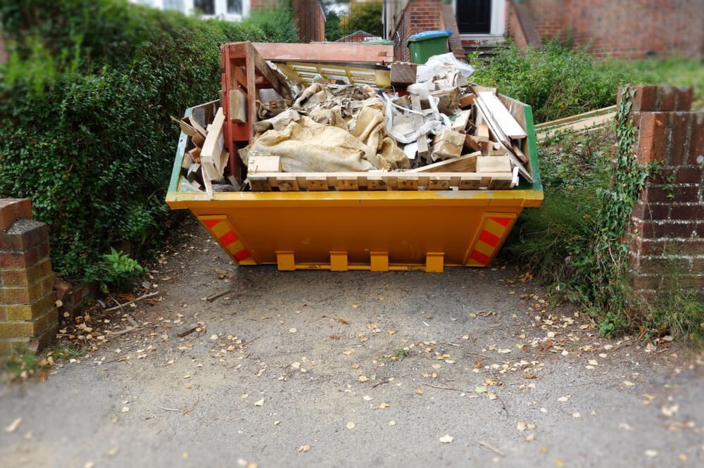 A Yellow Dumpster Filled With Junk is Parked in a Driveway — Swift Skips in Gympie, QLD