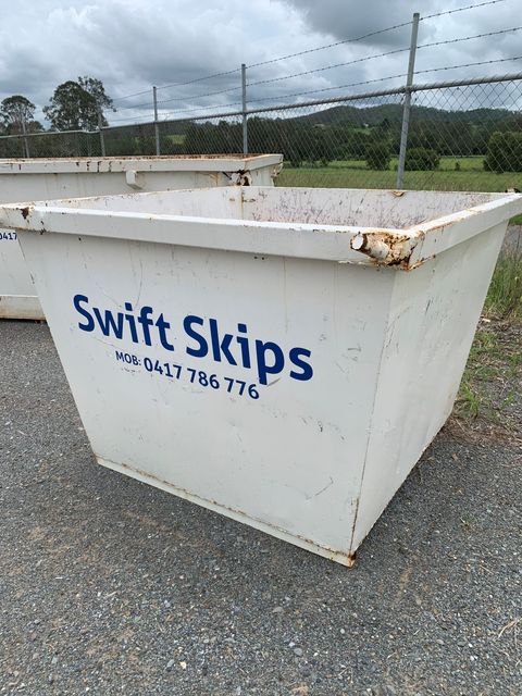 A White Skip Bin Is Sitting On The Sidewalk In Front Of A Building — Swift Skips in Gympie, QLD