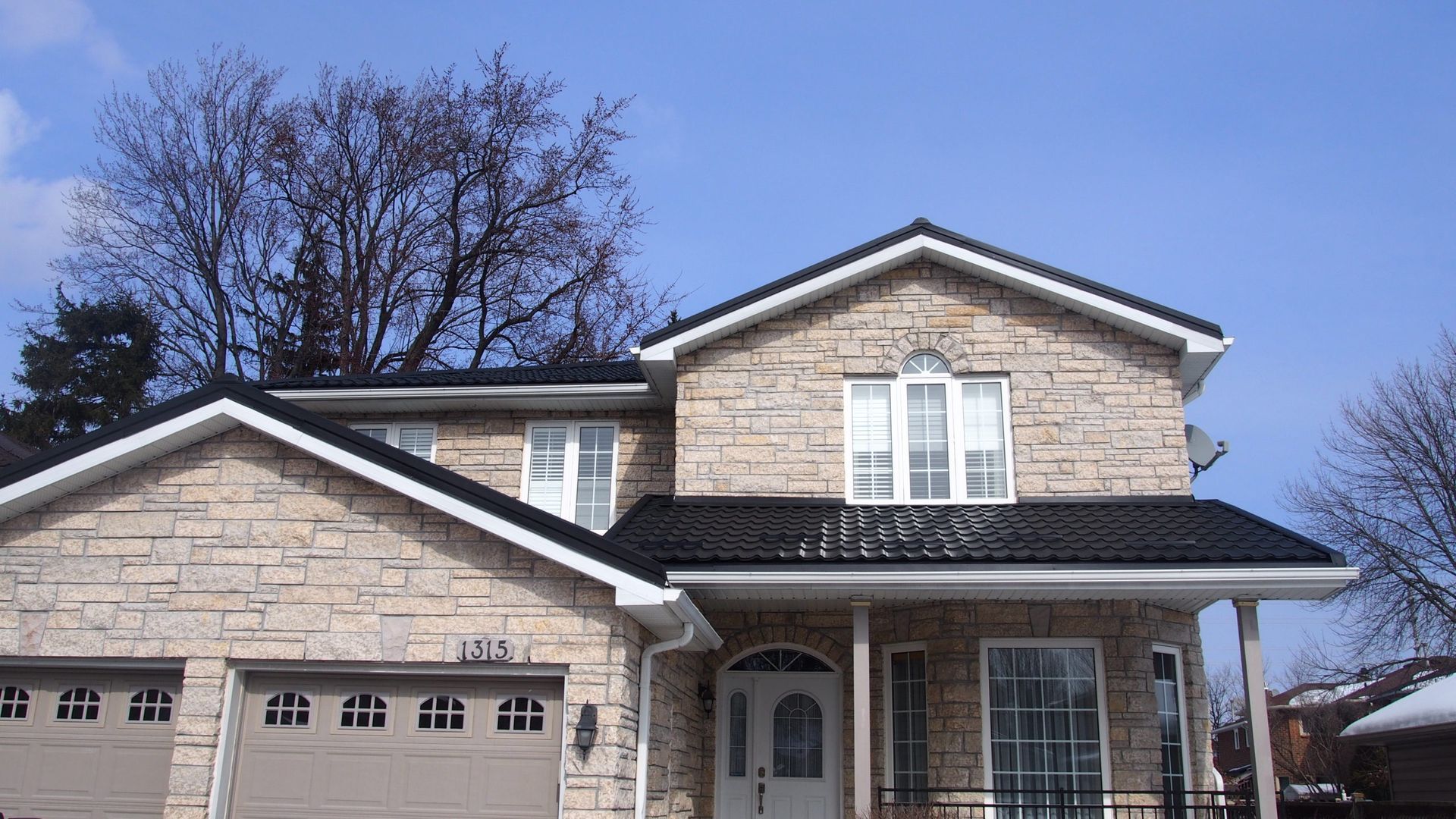 Une grande maison en briques avec un toit noir et deux portes de garage