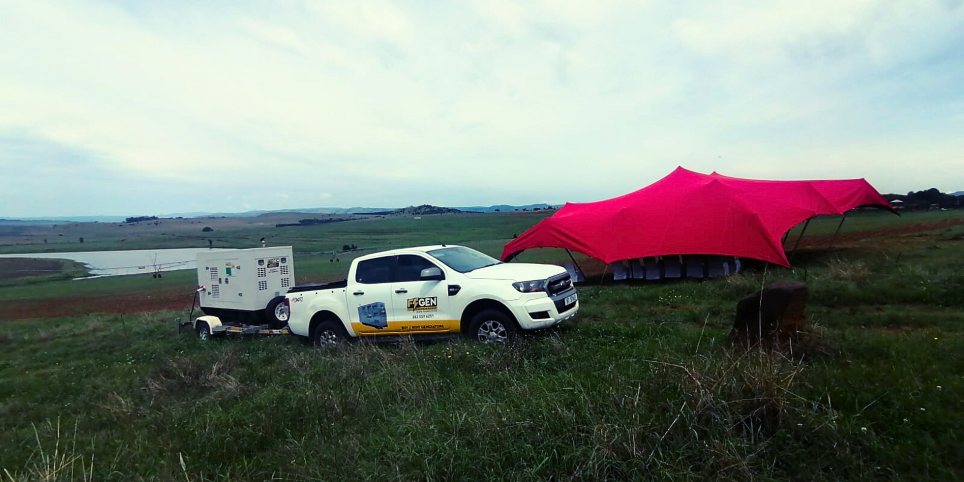 A white truck is parked in a grassy field next to a pink tent.
