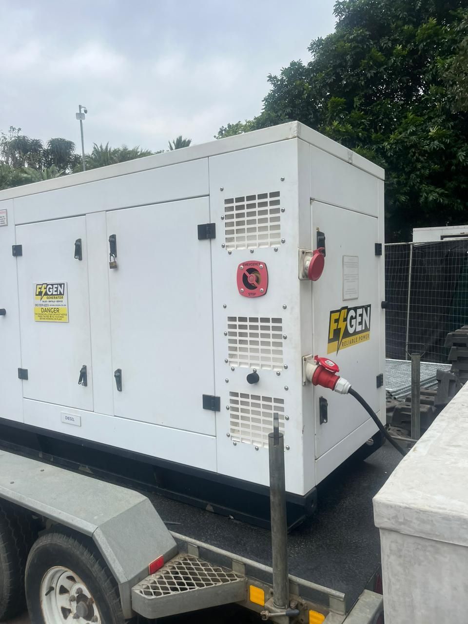 A large white generator is on a trailer with a fence in the background