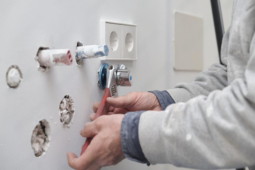 A plumber tightens plumbing fittings with a wrench to install water pipes in a newly constructed house.