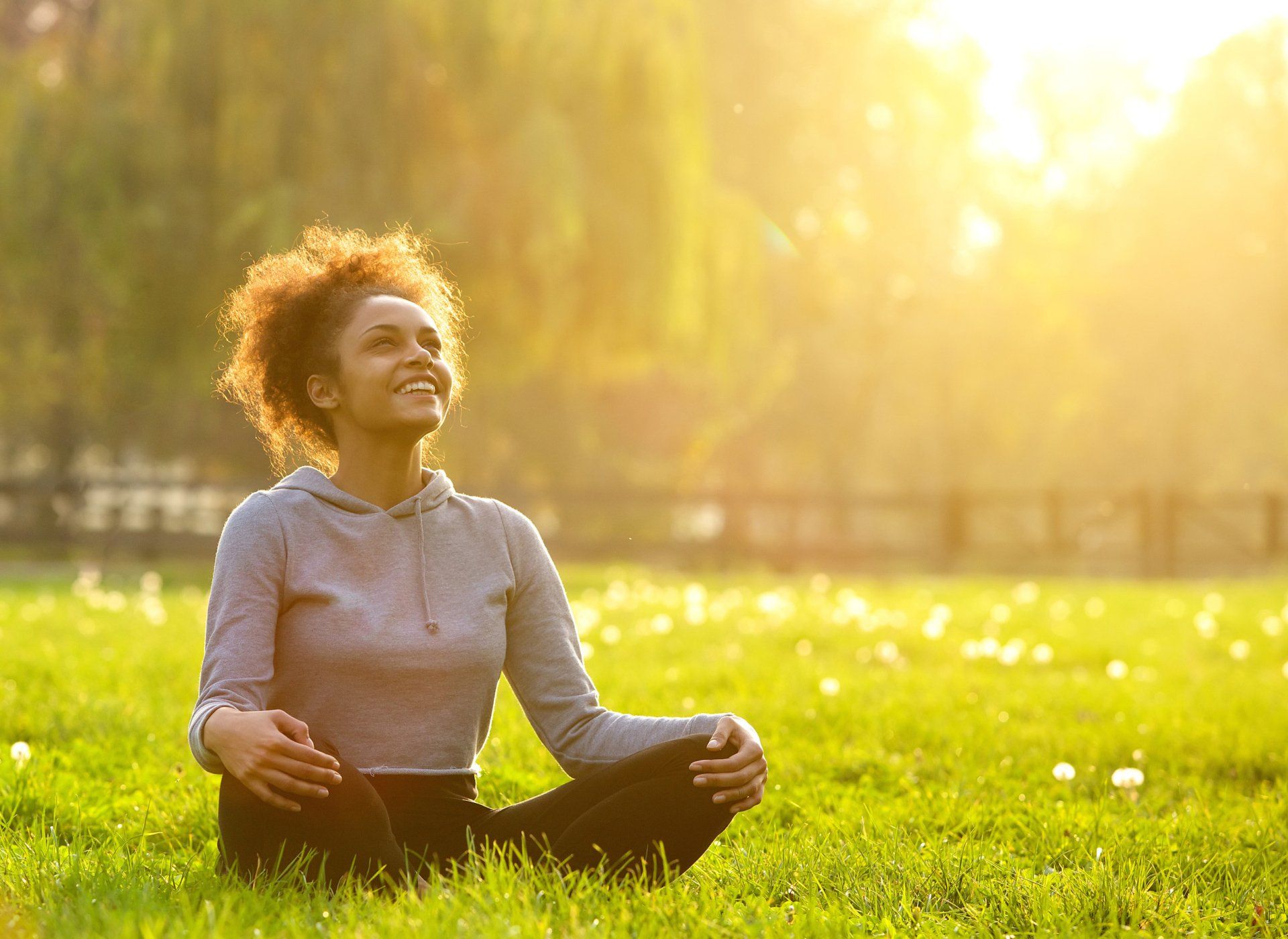 A woman is sitting in a lotus position on the grass in a park.
