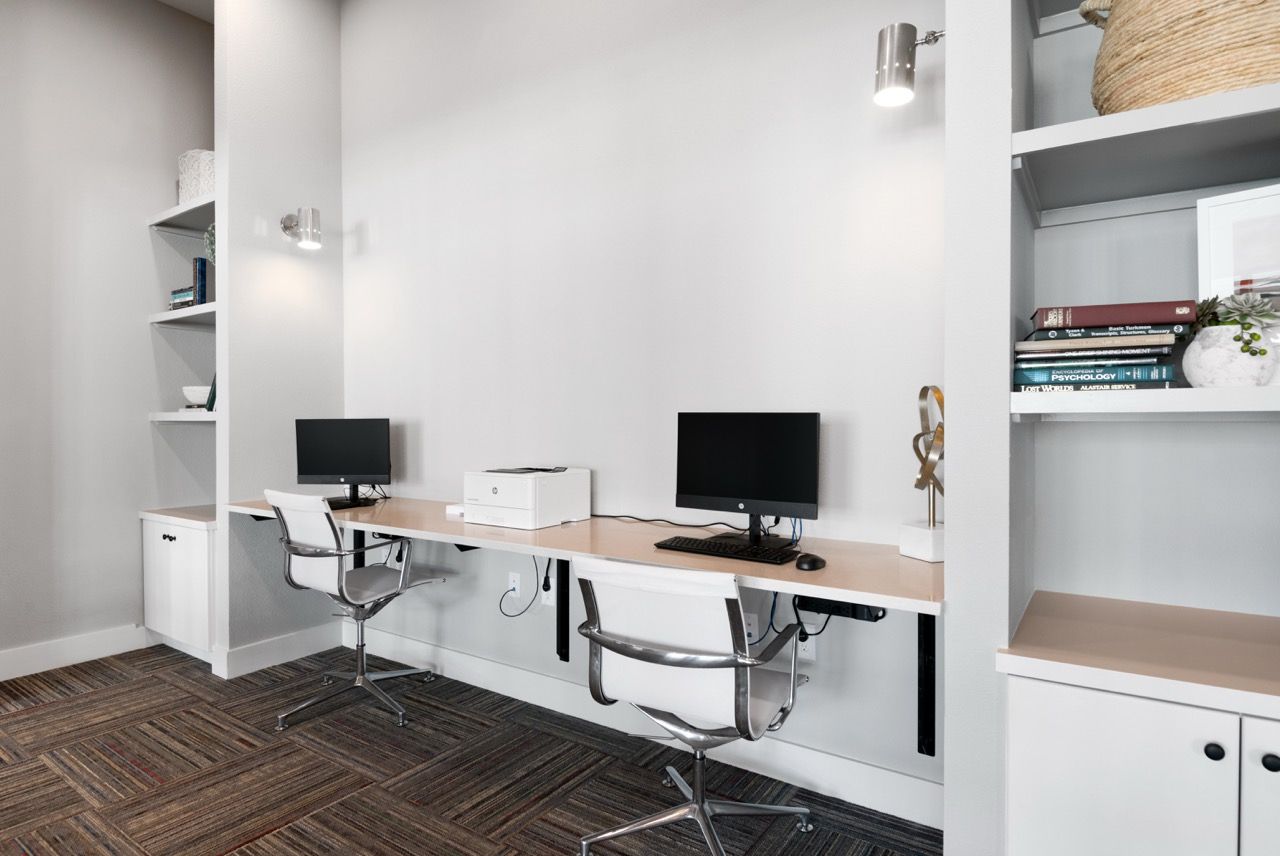 Home office area with a long desk, two computer setups, and built-in shelves.