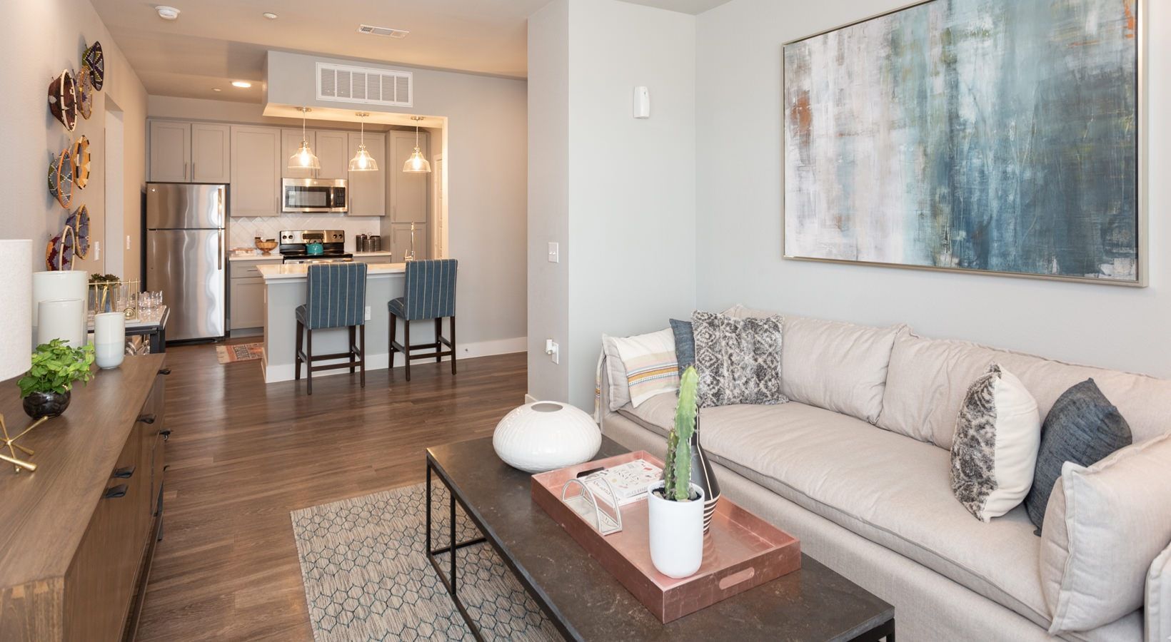 Open-concept living area with beige sofa, coffee table, and a kitchen island with bar stools.