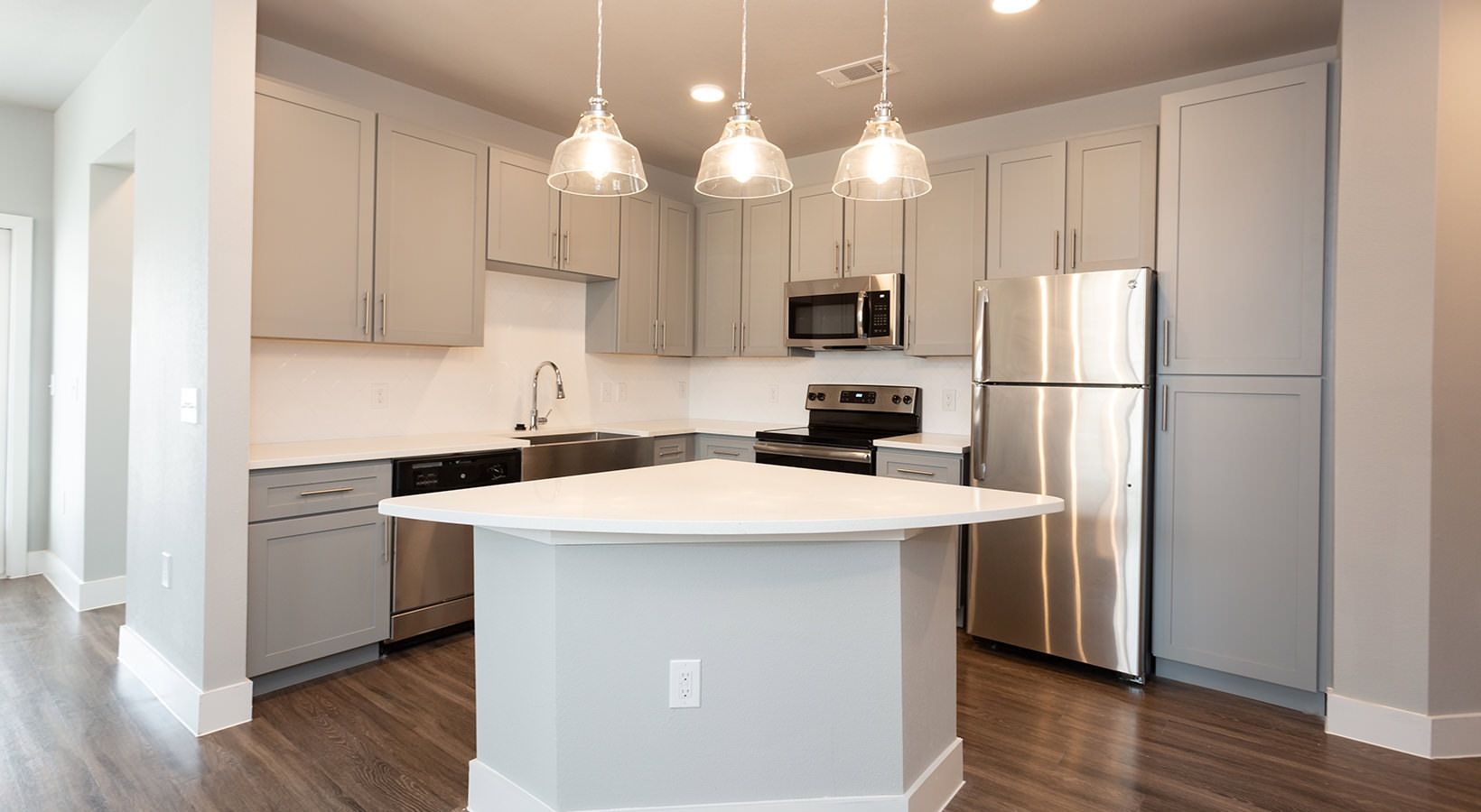 Modern kitchen with gray cabinets, stainless steel appliances, and a central island.