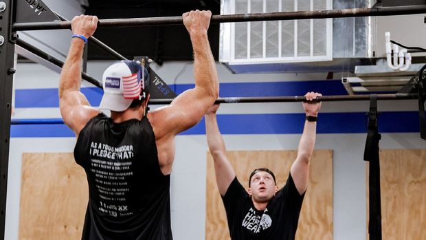 Two men are doing pull ups in a gym.