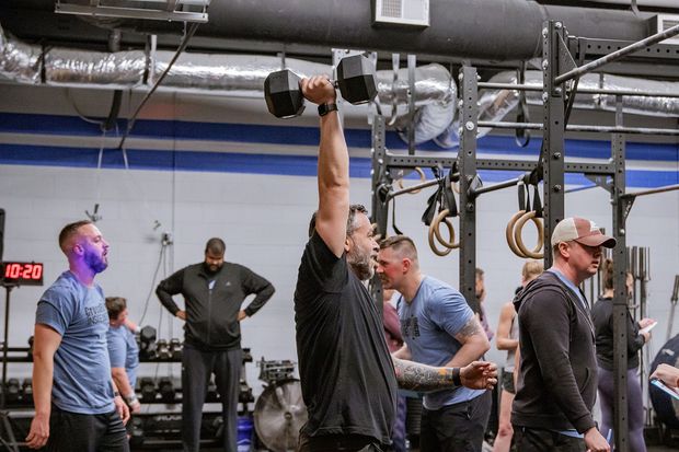 A man is lifting a dumbbell over his head in a gym.