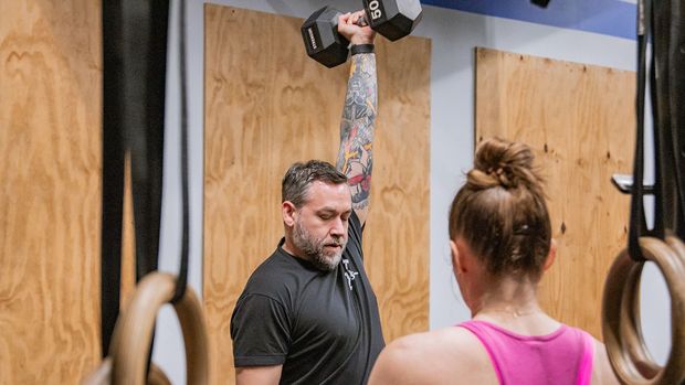 A man is lifting a dumbbell over a woman in a gym.