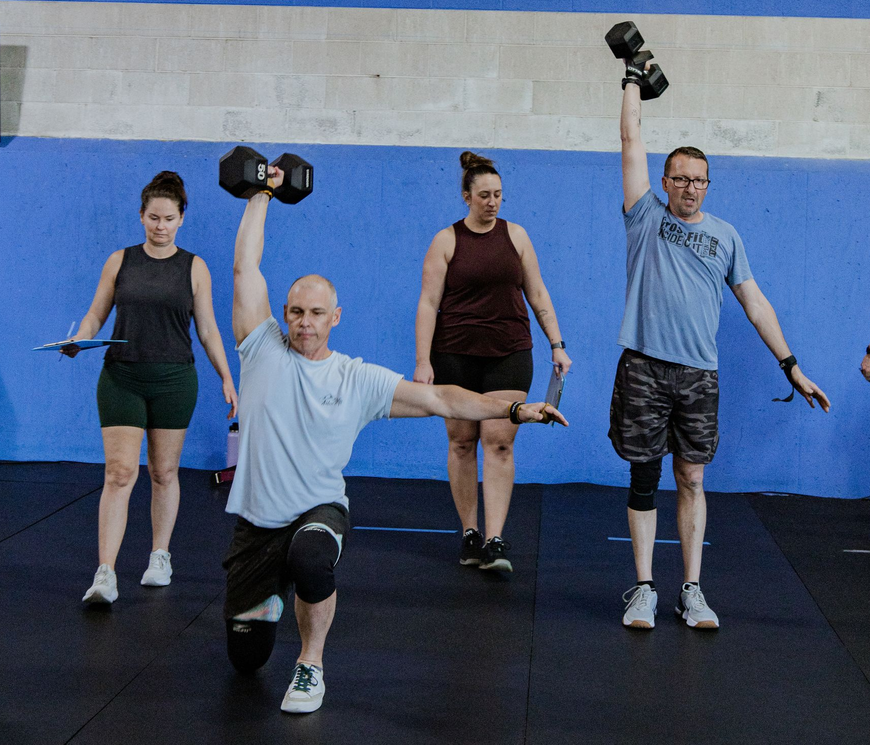A man is lifting a dumbbell over his head in a gym.