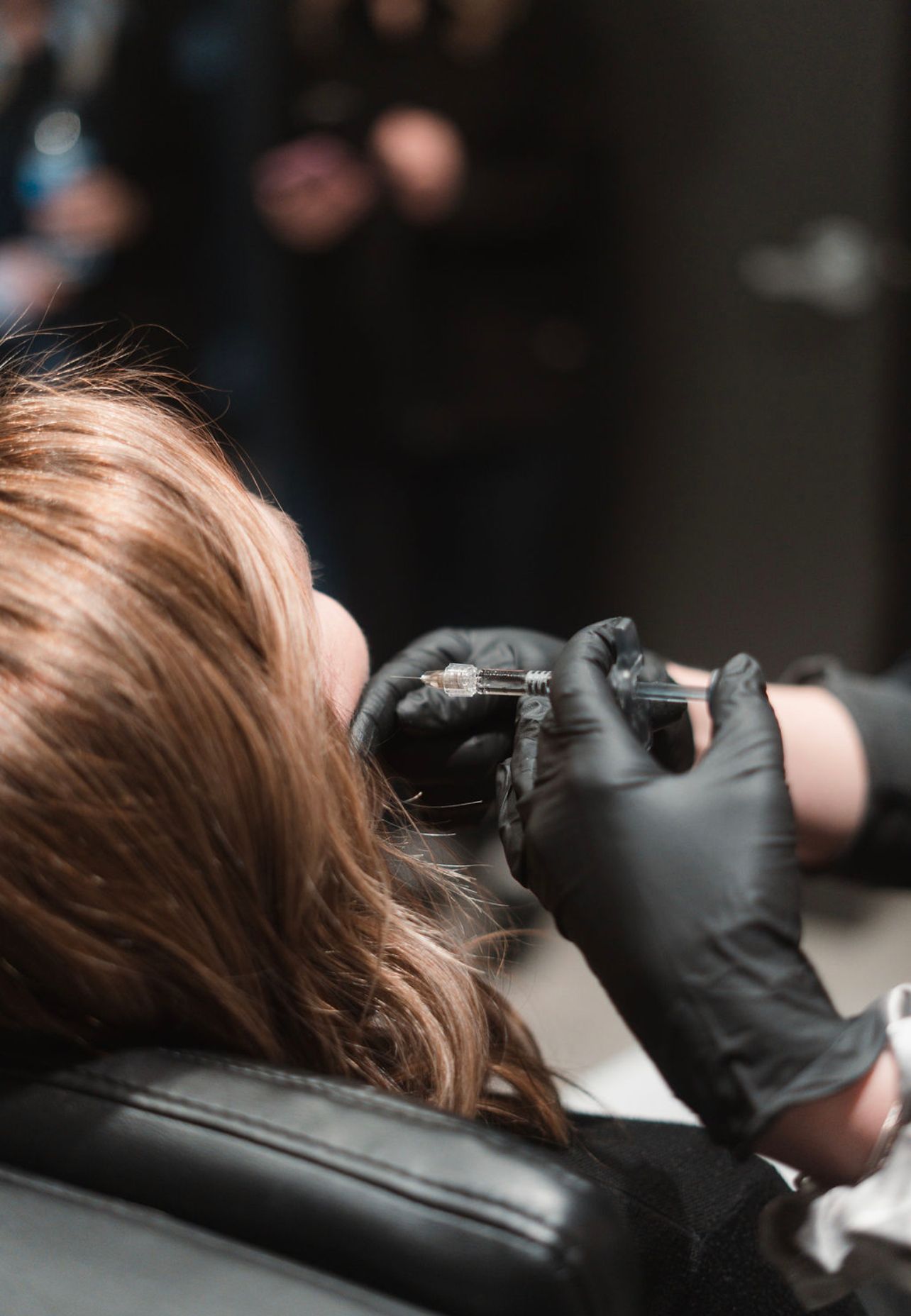 Woman receiving treatment on her forehead from a professional wearing gloves, near a golden lip sculpture.