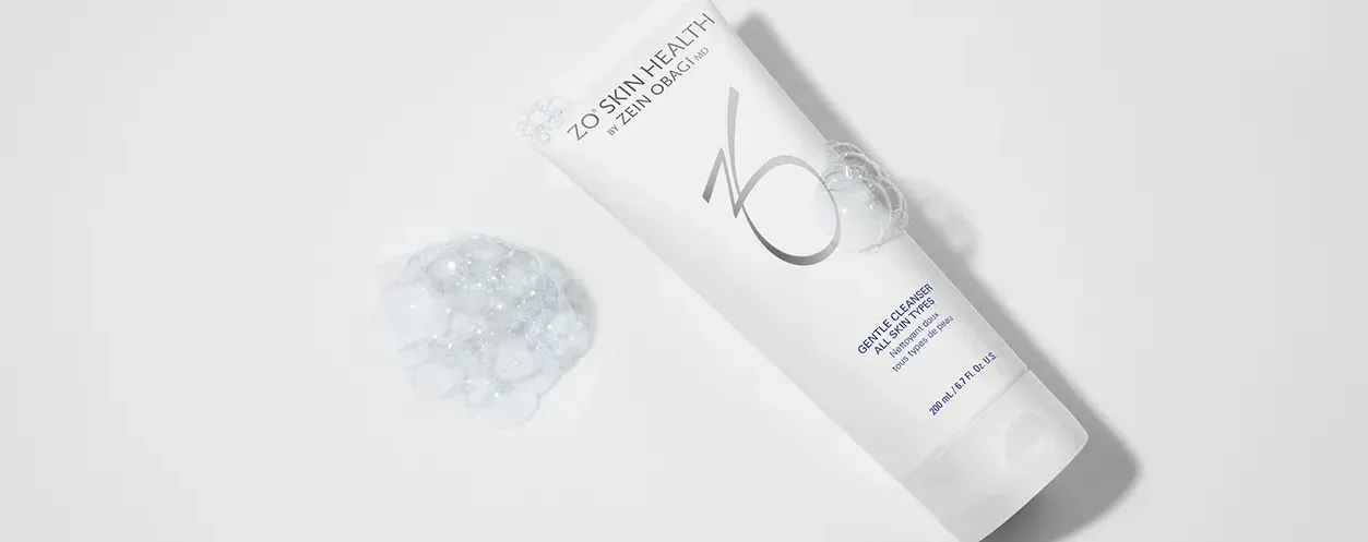 A white tube of facial cleanser with a glob of gel next to it, all on a white surface.