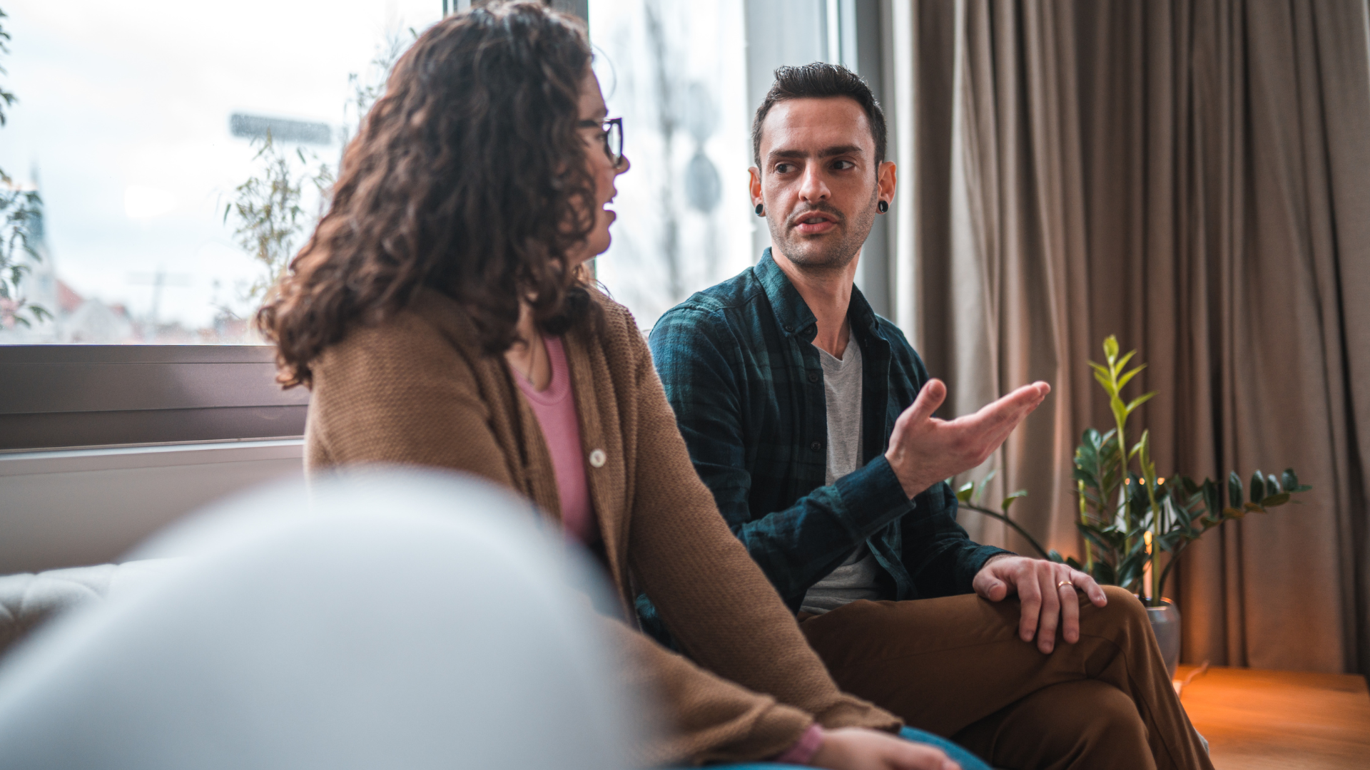 A man and a woman are sitting on a couch talking to each other.