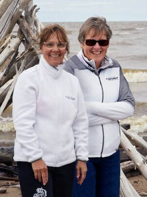 Two women are standing next to each other on the beach.