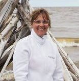 A woman in a white jacket is standing in front of a pile of driftwood.