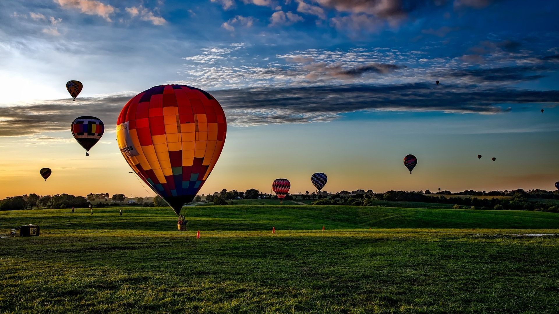 A group of hot air balloons are flying over a field at sunset.