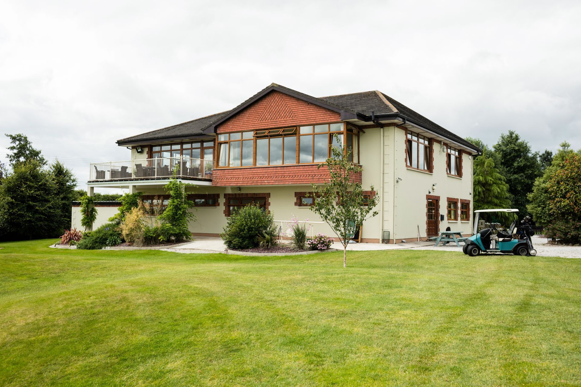 Large two-story house with balcony, surrounded by a lawn and trees, with a small golf cart nearby