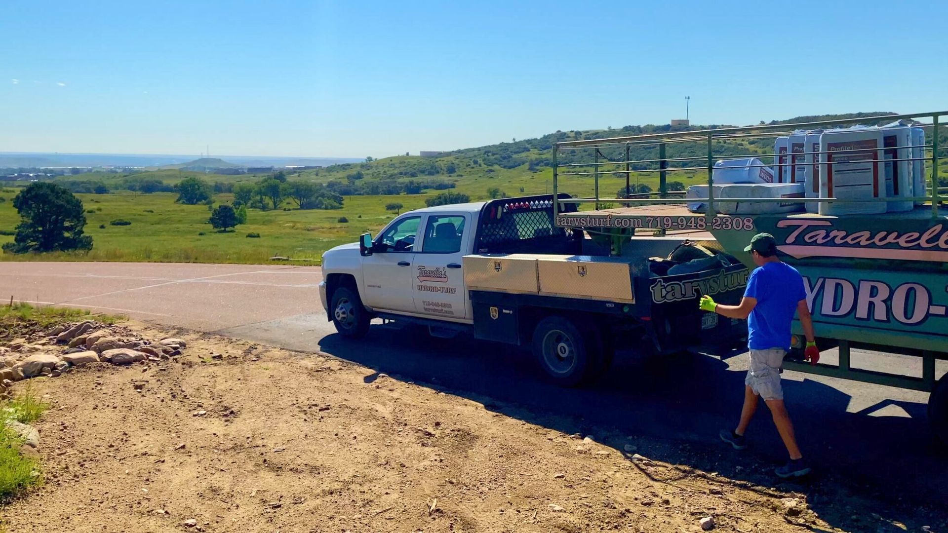 White pickup truck with trailer on a dirt road overlooking a green rural valley