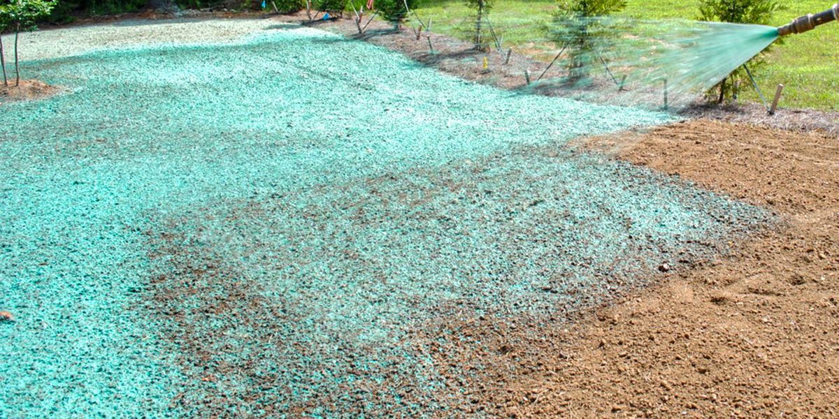 Large turquoise water spill spreading across a tan dirt path in an outdoor area