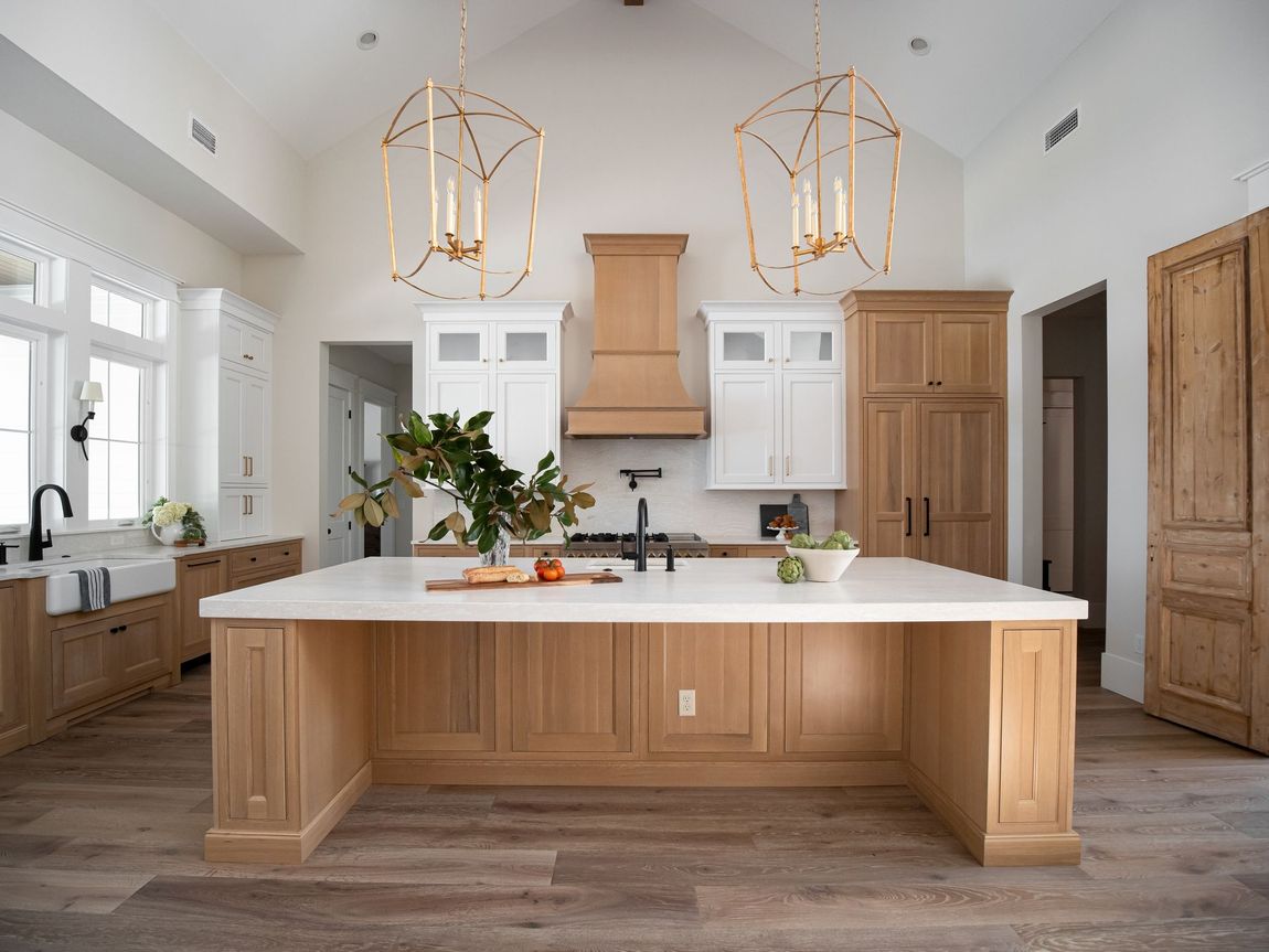 Bright, modern kitchen with a large wooden island, white cabinetry, gold pendant lights, and light wood flooring.
