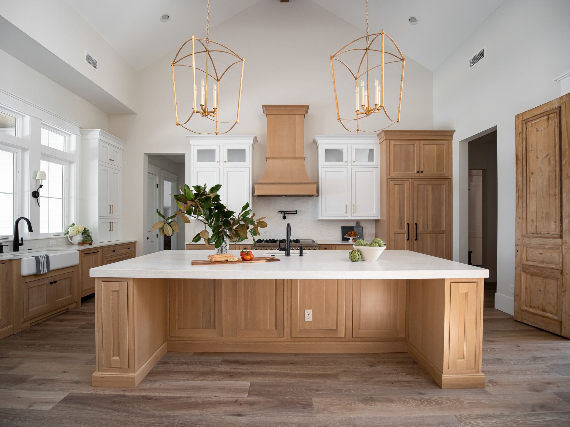 Bright, modern kitchen with a large wooden island, white cabinetry, gold pendant lights, and light wood flooring.